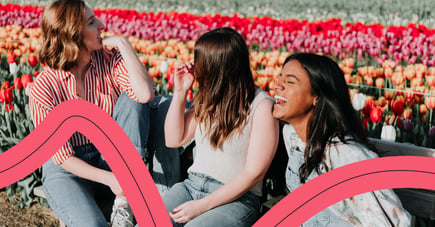 Three women sitting in a tulip field and laughing. 