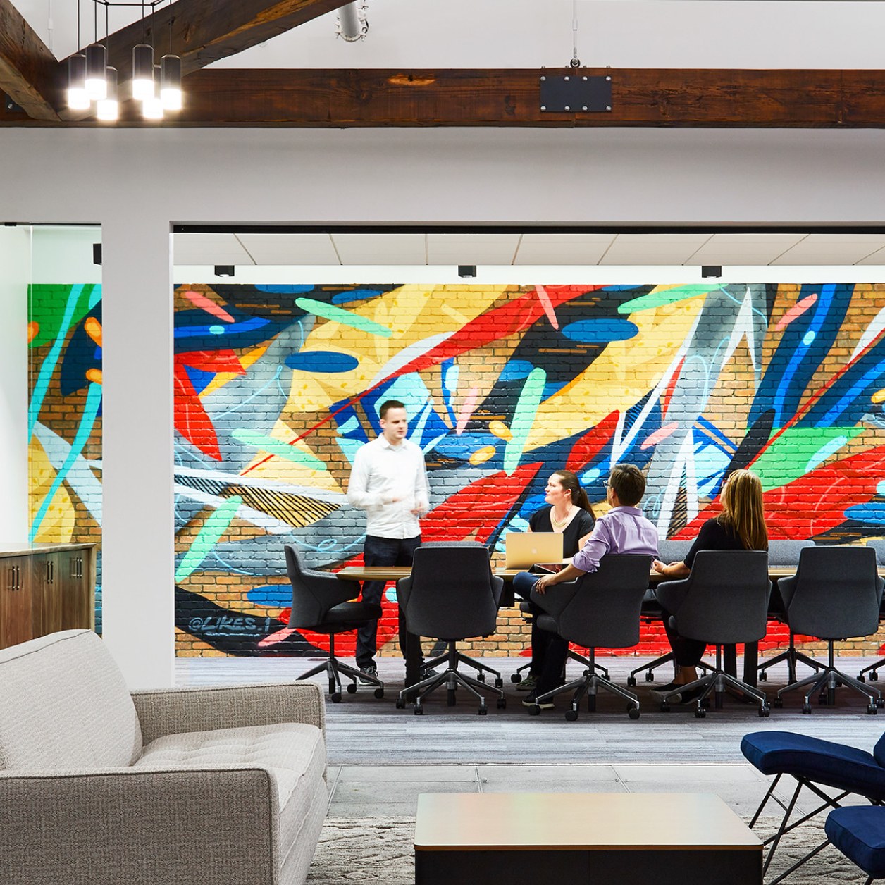 A group of people working at a desk with a colorful mural in the background.