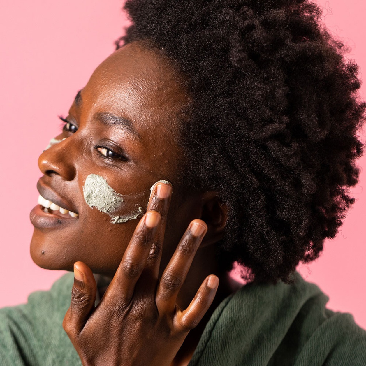 A woman applying a Lush face mask to her cheeks.